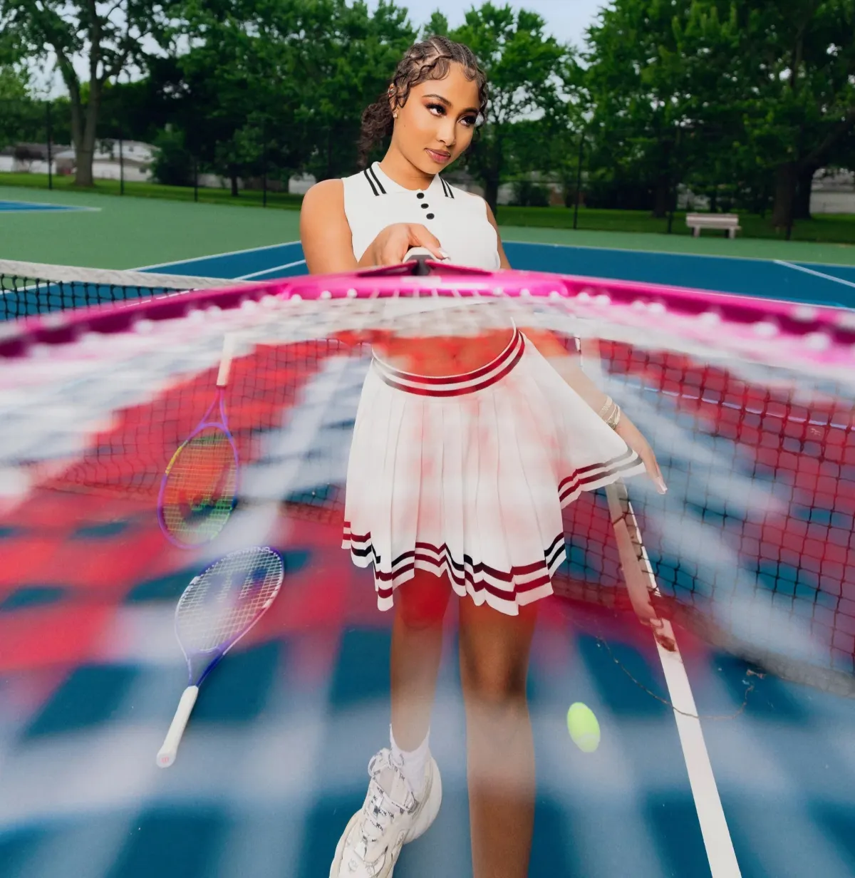 A woman in a white tennis outfit on a court, shot through the strings of a racket