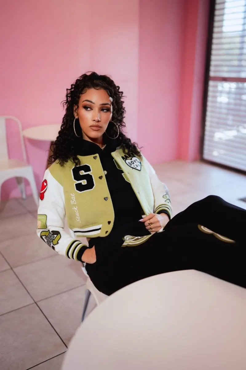 A model in a Stack Bae varsity jacket sitting in a pink room by a window