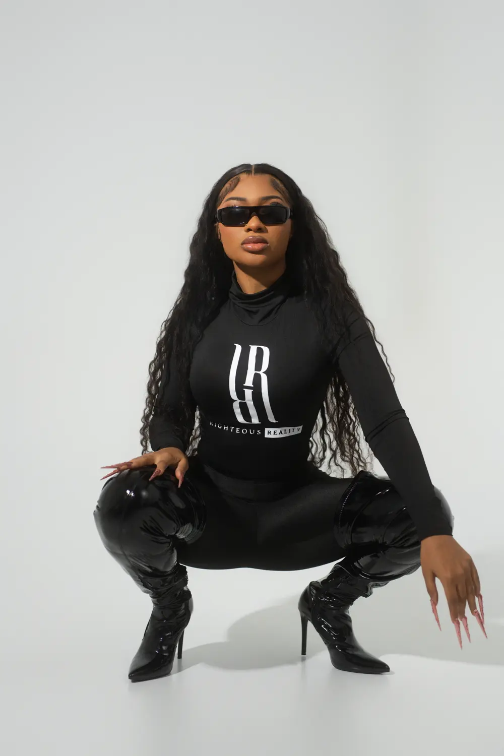 A model in a black Righteous Reality long sleeve and leather pants, crouching low in heels