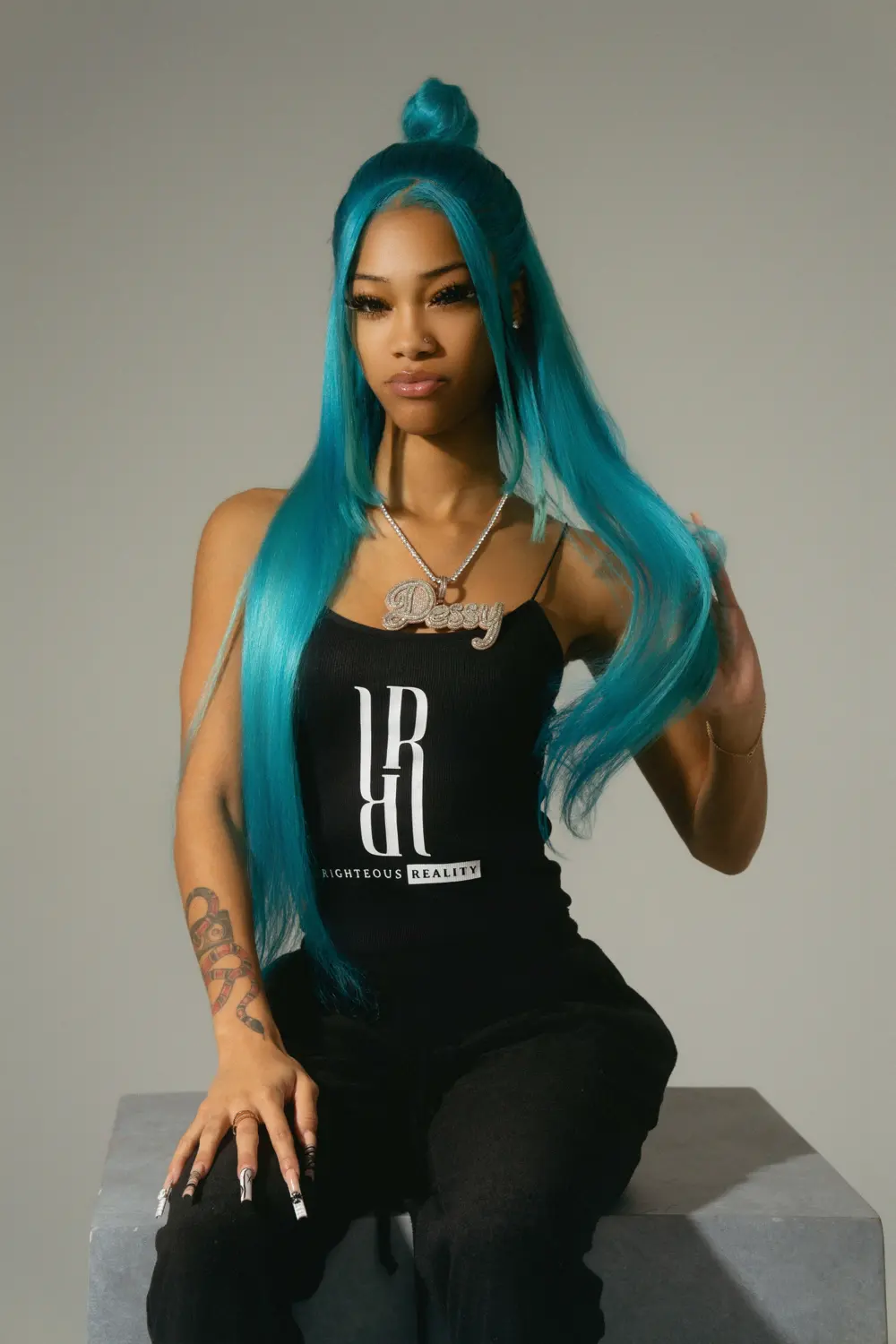 A model with turquoise hair in a black Righteous Reality tank top, looking straight at the camera